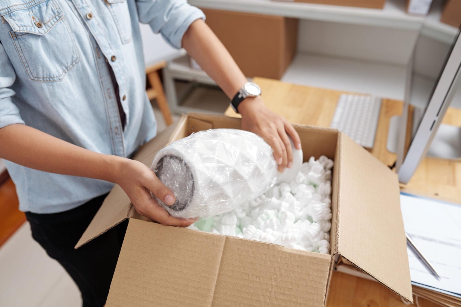 Person manually placing a wrapped item into a carton filled with styrofoam peanuts