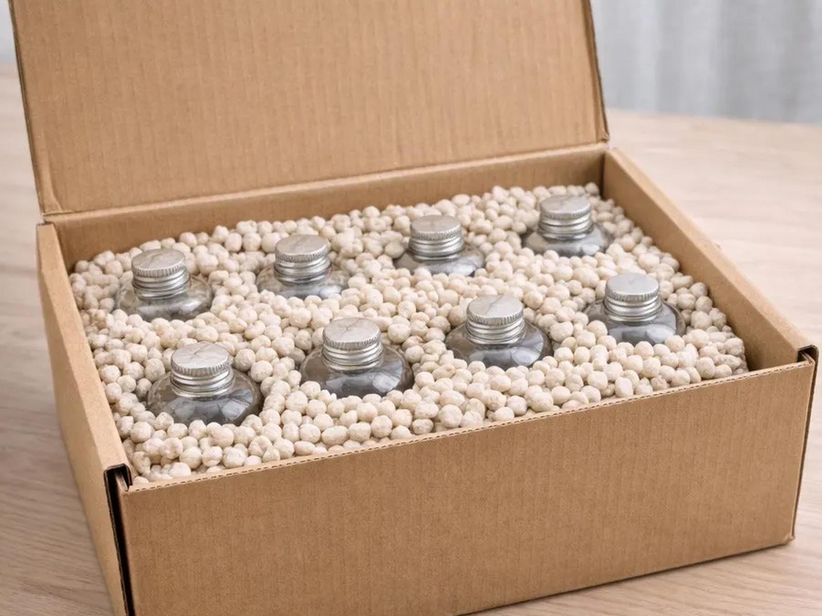 Open kraft carton with eight glass bottles cushioned by loose mycelium pellets filling the void